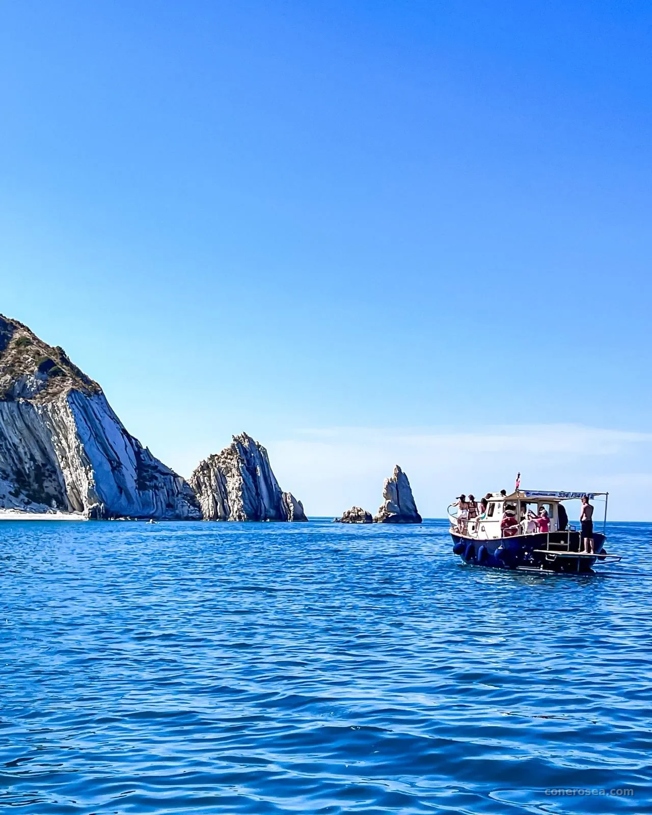 La barca di Conero Sea Tour in navigazione davanti alle falesie bianche e ai faraglioni del Conero